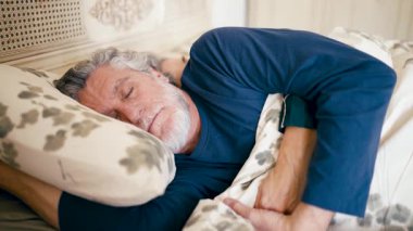 Gri saçlı ve sakallı yaşlı bir adam yatağında mışıl mışıl uyuyor. Evde uzun bir günün ardından yatak odasında dinlenen huzur dolu bir emekli.