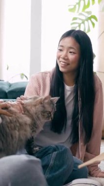 Kız arkadaşı kedilerini okşarken genç Asyalı kadın gülümsüyor. Güzel lezbiyen çift evlerinde dinleniyor. Dikey