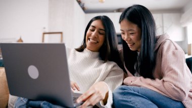 İki neşeli kadın bir anı paylaşıyor, dizüstü bilgisayarda gülümsüyor ve içeriği izlerken evdeki kanepede dinleniyorlar.