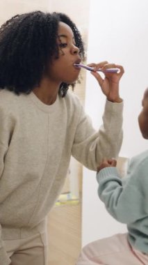 Sevgili Afrikalı Amerikalı anne kızına dişlerini nasıl fırçalayacağını gösteriyor. Mutlu aile banyoda günlük rutinlerini yapıyorlar. Dikey