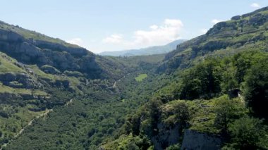 Derin, yemyeşil bir dağ vadisinde hareket eden nefes kesici hava görüntüleri. Açık mavi gökyüzünün altında kayalık kayalıklar ve yoğun ormanlar