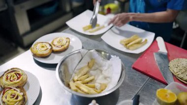 Profesyonel bir restoran mutfağında soslu hamburger ekmeğinin yanında maşa kullanarak yemek pişiriyor.