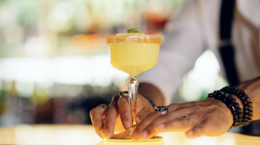 Barmen serinletici sarı bir kokteyl bardağını parlak bir tezgahın üzerine koyuyor.