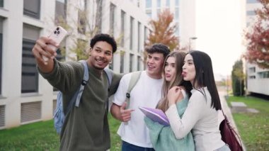 Dört genç ve neşeli üniversite öğrencisi akıllı telefonlarıyla komik bir grup selfie çekiyor. Çok ırklı arkadaşlar dışarıda eğleniyorlar.