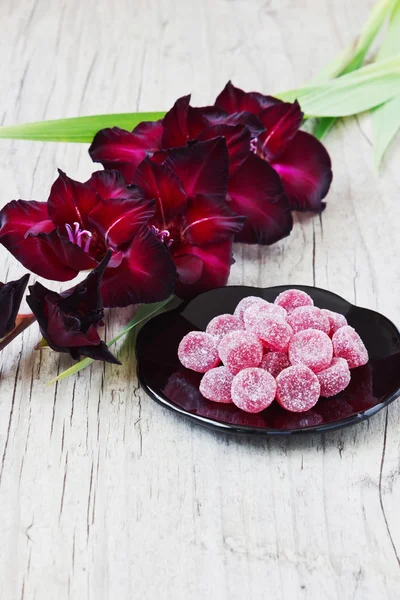 Candies and maroon gladiolus — Stock Photo, Image