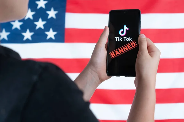 Nastolatek trzyma smartfona z logo Tiktok i na tle amerykańskiej flagi. Wybiórcze skupienie. Donald Trump zakazać Tiktok w Stanach Zjednoczonych. Rosja, Kazań - 08 sierpnia 2020 — Zdjęcie stockowe