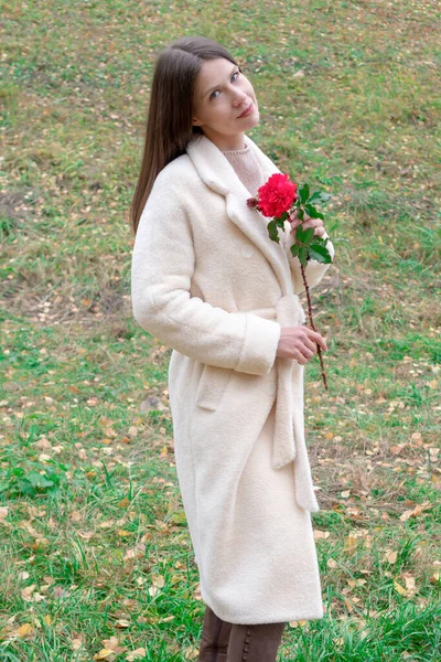Портрет молодой красивой женщины в стильном пальто с цветком в руках на фоне зеленой травы. Вертикальное фото — стоковое фото