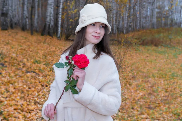 Portrait of a young beautiful woman in a stylish coat with a flower in her hands in the autumn forest. — Stock Photo, Image