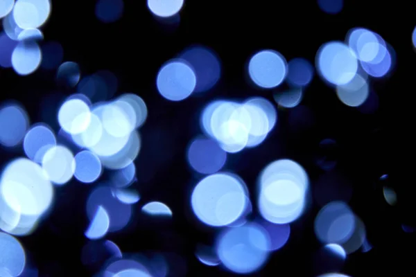 Odaklanamadığı Bokeh Noeli siyah arka planda büyük mavi ışıklar. Bulanık mavi parıltılı doku. Noel, yeni yıl ya da festival arka planı için mavi bokeh simli duvar kağıdı. 