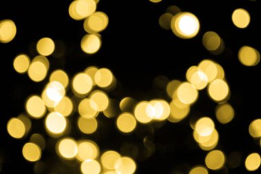 Odaklanamayan Bokeh Noel 'i siyah arka planda büyük altın ışıklar. Soyut, bulanık altın parıltısı dokusu. Noel, yeni yıl ya da festival arka planı için altın parlayan duvar kağıdı.