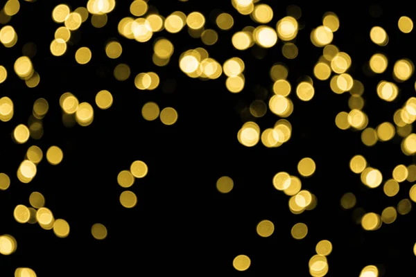 A lot of defocused bokeh christmas small gold lights on black background. Blurred abstract gold glitter texture. Gold bokeh glitter wallpaper for Christmas, New year or festival background.