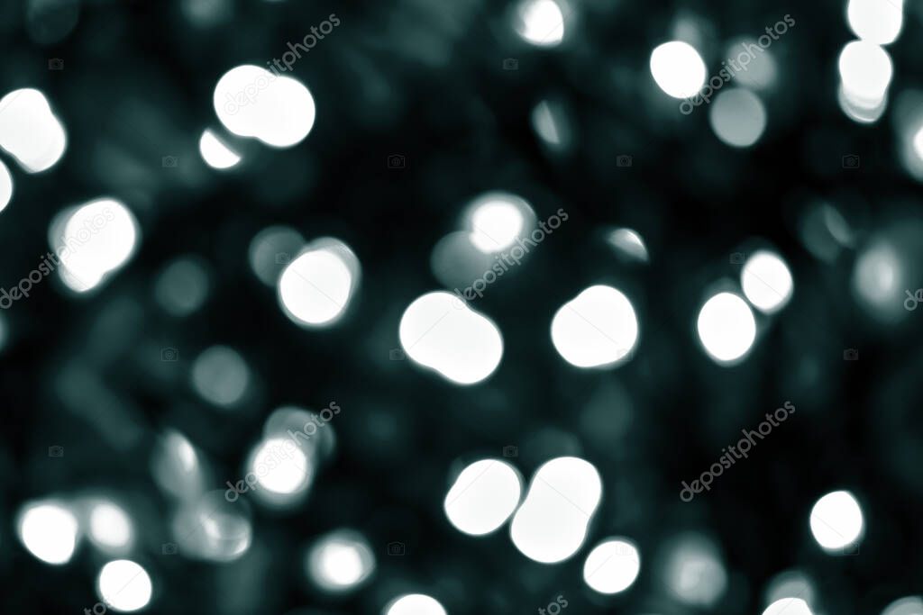 A lot of defocused bokeh christmas big white  lights on dark background. Blurred abstract green glitter texture. Green bokeh glitter wallpaper for Christmas, New year or festival background. Tidewater Green colors.