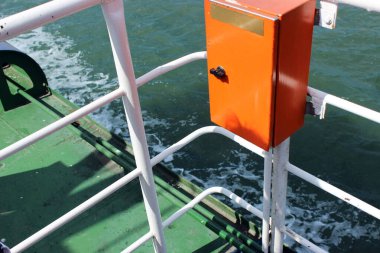 Denizde giden feribotun görüntüsü. Fotoğrafta mavi-yeşil deniz suyu, köpük dalgaları, feribot ekipmanları, tırabzanlar görülüyor. Güneşli bir günde, güzel bir deniz havasıyla denize bir gezi..