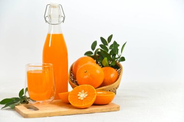 Taze sıkılmış portakal suyu bardakta, dolu bir şişe ve dilimlenmiş portakallar beyaz arka planda..