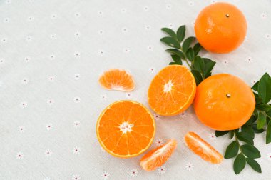 Organik bütün portakallar, ince dilimler, segmentler ve canlı renkli yapraklar beyaz çiçek desenli kumaş arkaplanda düzenlenir..