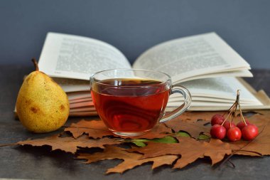 Bir fincan sıcak çay, sonbahar yaprakları ve ahşap arka planda meyveler. Kitaplar, böğürtlenler, armutlar. Ev konforu. Sonbahar havası. Seçici odaklanma. Boşluğu kopyala