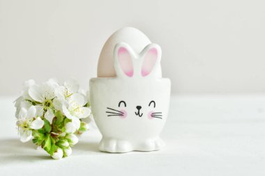 Tatlı tavşanlı ve beyaz masa arkasında taze çiçekler olan Paskalya bayramın kutlu olsun. Tebrik kartı. Paskalya geçmişi. Kopyala lütfen. Seçici odak