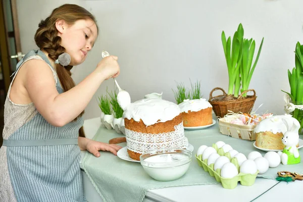 Smiling Girl with bunny ears covers easter cake with icing.Preparation to easter.Easter cake with green grass. Homemade pasques.Easter sweets on white background.copy space.Selective focus