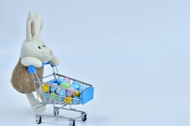 Beyaz arka planda çok renkli paskalya yumurtaları olan bir alışveriş arabası. Paskalya satışı. Paskalya tavşanı ve alışveriş arabası. Kopya alanı. Seçici odak