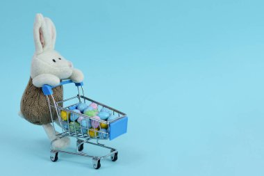 Mavi arka planda çok renkli paskalya yumurtaları olan bir alışveriş arabası. Paskalya satışı. Paskalya tavşanı ve alışveriş arabası. Kopya alanı. Seçici odak