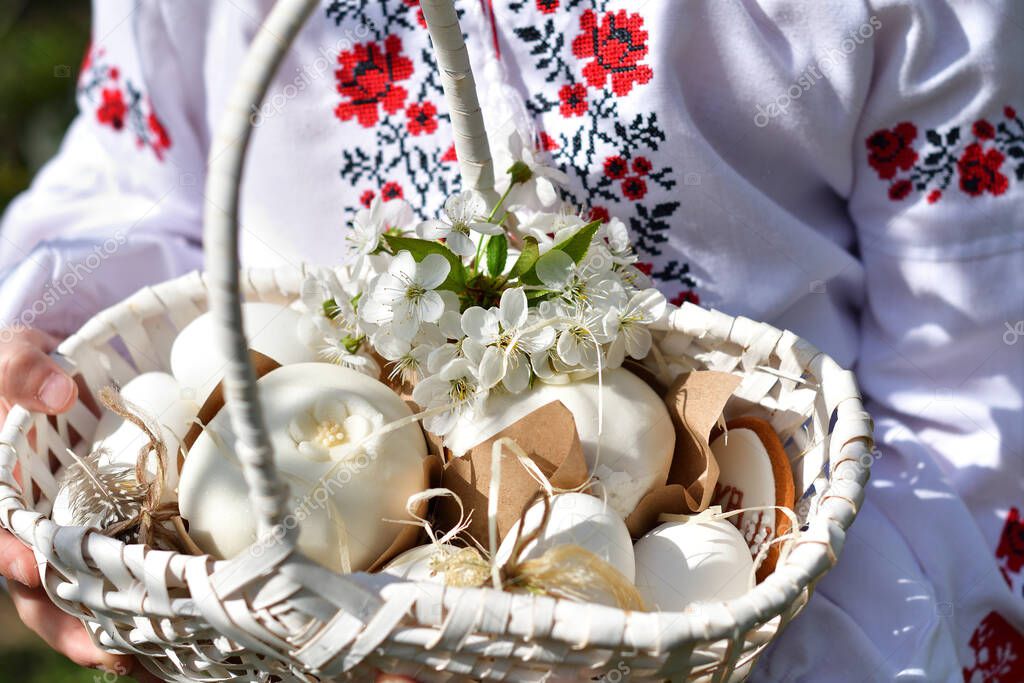 girl in a traditional embroidered shirt in a blooming cherry garden.Kid with colored eggs and traditional Easter Cake in basket. Happy Easter day, Christian traditions.Copy space.Soft focus