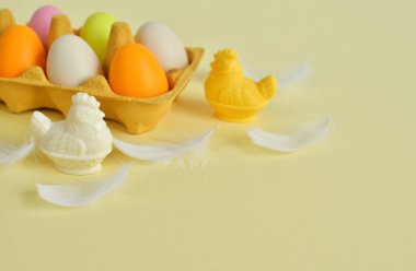 Sarı karton tepside renkli yumurtalar ve beyaz tüy. Paskalya dekorasyonları, kompozisyon. kopyalama alanı. Seçici odak