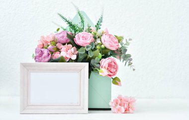Krem rengi fotoğraf çerçevesi, parlak arka planda pembe güller. Çiçek şenliği fotoğrafı. Çiçeklerle dolu rahat bir ev. Boşluğu kopyala