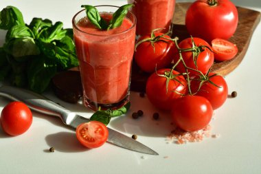 Çiğ domates ve yeşil fesleğen yapraklarıyla süslenmiş iki bardak taze organik domates suyu. Sağlıklı beslenme kavramı. Kopya alanı. Seçici odak