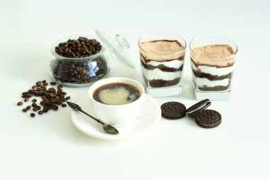 Bir fincan sade kahve ve kahve çekirdeği, bardakta tatlı. Çikolatalı cheesecake ve beyaz arka planda süzme peynir kremi. Günaydın konsepti. Uzayı kopyala Seçici odak.