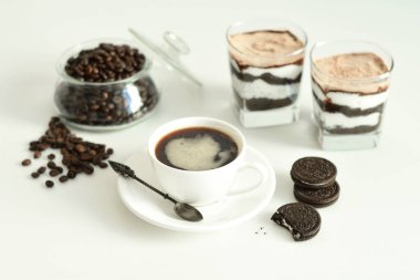 Bir fincan sade kahve ve kahve çekirdeği, bardakta tatlı. Çikolatalı cheesecake ve beyaz arka planda süzme peynir kremi. Günaydın konsepti. Uzayı kopyala Seçici odak.