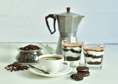 Bir fincan sade kahve ve kahve çekirdeği, bardakta tatlı. Çikolatalı cheesecake ve beyaz arka planda süzme peynir kremi. Günaydın konsepti. Uzayı kopyala Seçici odak.