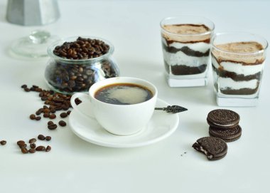 Bir fincan sade kahve ve kahve çekirdeği, bardakta tatlı. Çikolatalı cheesecake ve beyaz arka planda süzme peynir kremi. Günaydın konsepti. Uzayı kopyala Seçici odak.