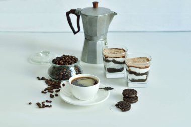 Bir fincan sade kahve ve kahve çekirdeği, bardakta tatlı. Çikolatalı cheesecake ve beyaz arka planda süzme peynir kremi. Günaydın konsepti. Uzayı kopyala Seçici odak.