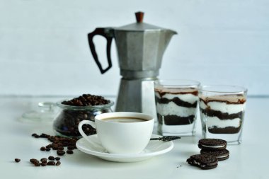 Bir fincan sade kahve ve kahve çekirdeği, bardakta tatlı. Çikolatalı cheesecake ve beyaz arka planda süzme peynir kremi. Günaydın konsepti. Uzayı kopyala Seçici odak.