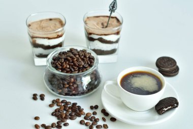 Bir fincan sade kahve ve kahve çekirdeği, bardakta tatlı. Çikolatalı cheesecake ve beyaz arka planda süzme peynir kremi. Günaydın konsepti. Uzayı kopyala Seçici odak.