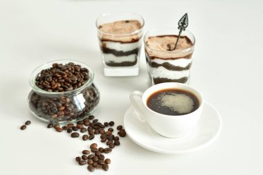 Bir fincan sade kahve ve kahve çekirdeği, bardakta tatlı. Çikolatalı cheesecake ve beyaz arka planda süzme peynir kremi. Günaydın konsepti. Uzayı kopyala Seçici odak.