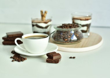 Bir fincan sade kahve ve kahve çekirdeği, bardakta tatlı. Çikolatalı cheesecake ve beyaz arka planda süzme peynir kremi. Günaydın konsepti. Uzayı kopyala Seçici odak.