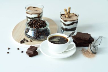 Bir fincan sade kahve ve kahve çekirdeği, bardakta tatlı. Çikolatalı cheesecake ve beyaz arka planda süzme peynir kremi. Günaydın konsepti. Uzayı kopyala Seçici odak.