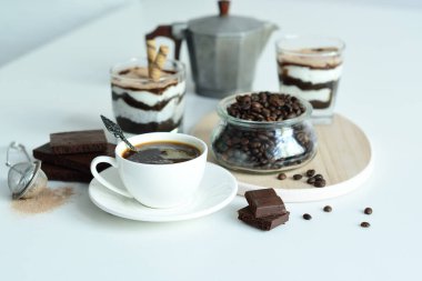 Bir fincan sade kahve ve kahve çekirdeği, bardakta tatlı. Çikolatalı cheesecake ve beyaz arka planda süzme peynir kremi. Günaydın konsepti. Uzayı kopyala Seçici odak.