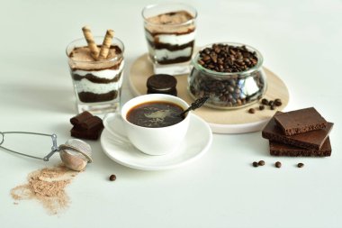 Bir fincan sade kahve ve kahve çekirdeği, bardakta tatlı. Çikolatalı cheesecake ve beyaz arka planda süzme peynir kremi. Günaydın konsepti. Uzayı kopyala Seçici odak.