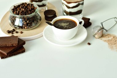 Bir fincan sade kahve ve kahve çekirdeği, bardakta tatlı. Çikolatalı cheesecake ve beyaz arka planda süzme peynir kremi. Günaydın konsepti. Uzayı kopyala Seçici odak.