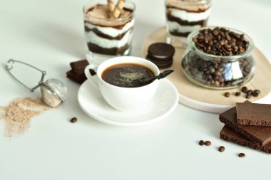 Bir fincan sade kahve ve kahve çekirdeği, bardakta tatlı. Çikolatalı cheesecake ve beyaz arka planda süzme peynir kremi. Günaydın konsepti. Uzayı kopyala Seçici odak.