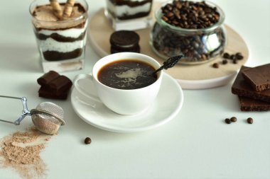 Bir fincan sade kahve ve kahve çekirdeği, bardakta tatlı. Çikolatalı cheesecake ve beyaz arka planda süzme peynir kremi. Günaydın konsepti. Uzayı kopyala Seçici odak.