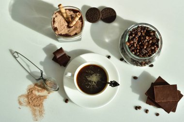 Bir fincan sade kahve ve kahve çekirdeği, bardakta tatlı. Çikolatalı cheesecake ve beyaz arka planda süzme peynir kremi. Günaydın konsepti. Uzayı kopyala Seçici odak.