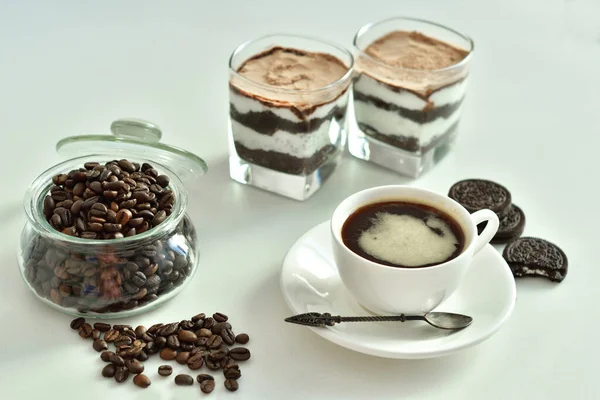 Bir fincan sade kahve ve kahve çekirdeği, bardakta tatlı. Çikolatalı cheesecake ve beyaz arka planda süzme peynir kremi. Günaydın konsepti. Uzayı kopyala Seçici odak.