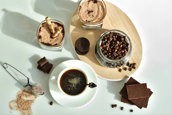 Bir fincan sade kahve ve kahve çekirdeği, bardakta tatlı. Çikolatalı cheesecake ve beyaz arka planda süzme peynir kremi. Günaydın konsepti. Uzayı kopyala Seçici odak.