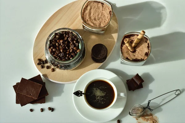 Bir fincan sade kahve ve kahve çekirdeği, bardakta tatlı. Çikolatalı cheesecake ve beyaz arka planda süzme peynir kremi. Günaydın konsepti. Uzayı kopyala Seçici odak.