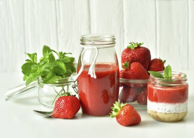 Cam kavanozda çilek ve krem peynirli ev yapımı çok katmanlı tatlı. Olgun yeşil limon ve beyaz arka planda nane. seçici odak