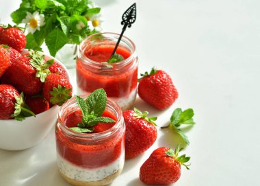 Cam kavanozda çilek ve krem peynirli ev yapımı çok katmanlı tatlı. Olgun yeşil limon ve beyaz arka planda nane. seçici odak