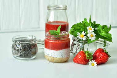 Çilekli ev yapımı peynirli kek ve cam kavanozda süzme peynir kremi. Taze yeşil limon, beyaz arka planda nane ve chia. Seçici odak noktası.